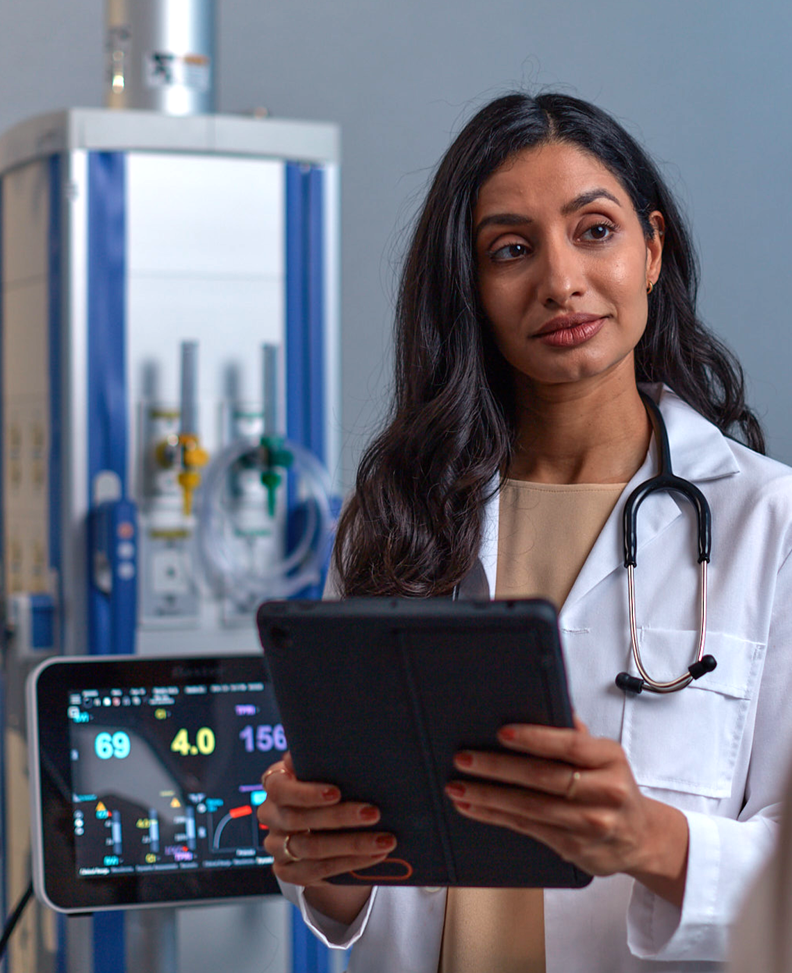 Healthcare professional holding a tablet with medical device in the background